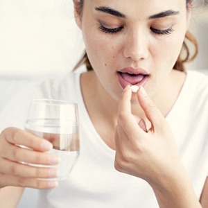 A woman taking a painkiller with water.