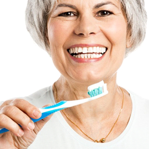 An older woman holding a toothbrush and smiling.