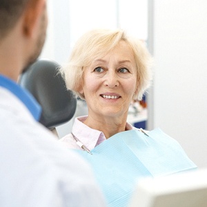 Older woman smiling while sitting in dental chair looking at dentist