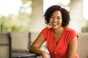 Woman in orange smiling while sitting at a table outside