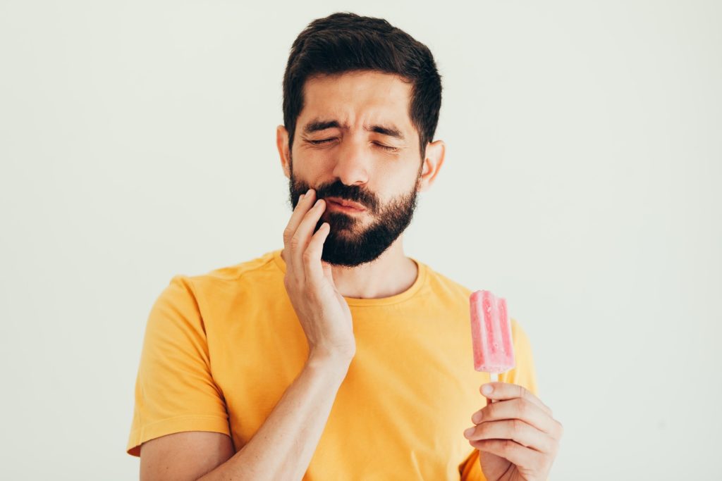 Man experiencing dental implant sensitivity while eating a popsicle