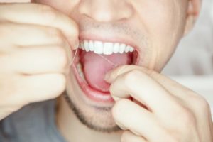 Close up of a man using dental floss.