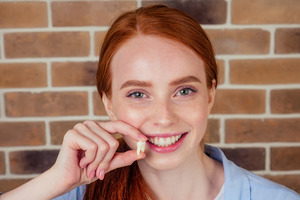 Red-haired woman holding up wisdom tooth after extraction