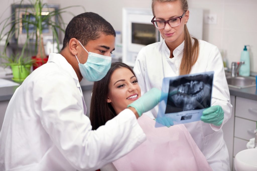 patient looking at X-ray of wisdom teeth with dentists