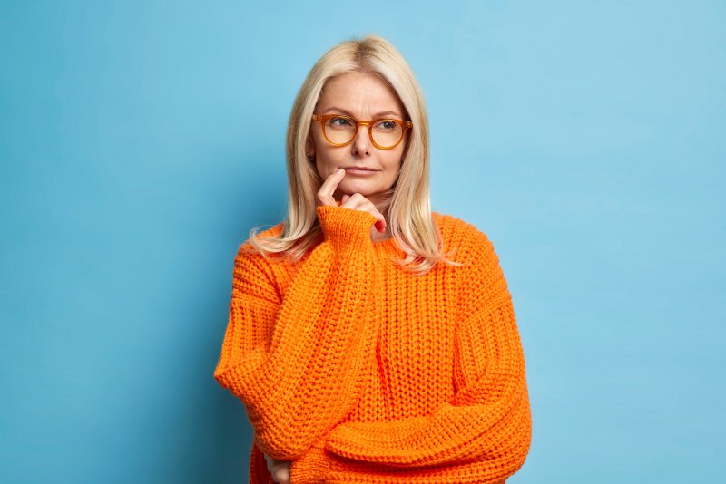 a woman in glasses thinking about dental implants