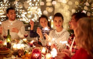 Group of people around a dinner table full of holiday foods with sparklers